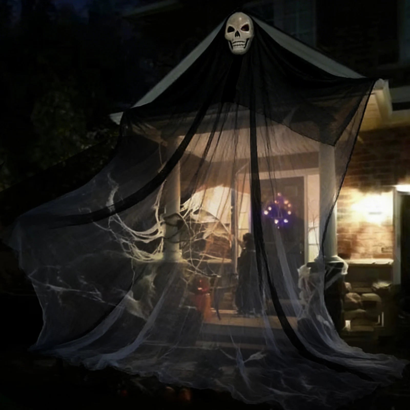 A themed setting presents 10-foot lighted black hanging skeleton ghost displayed outside a home, with the skull head, wide black gauze and long hanging silhouette clearly visible.