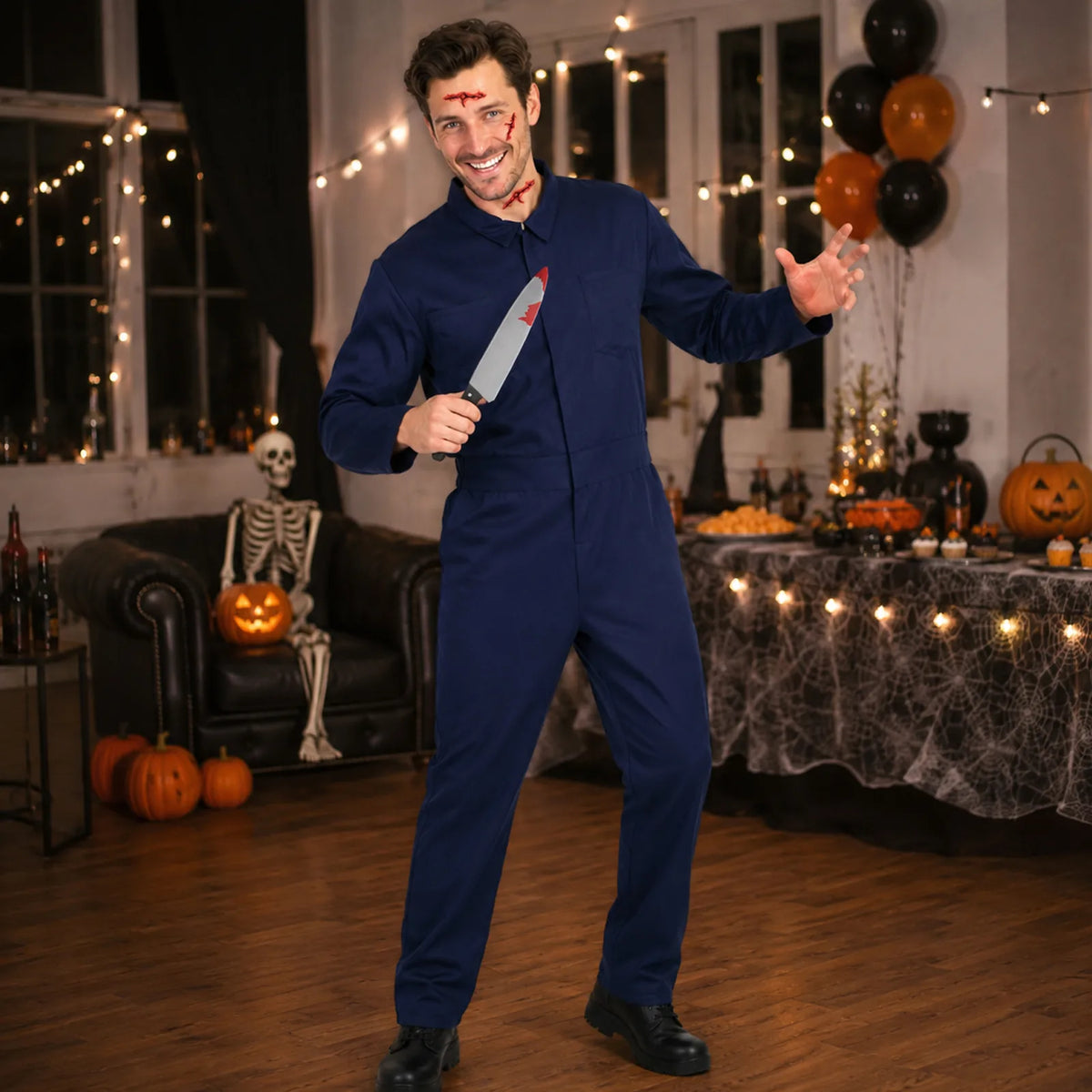 An unmasked man wears navy coveralls and wound-effect stickers while holding a costume knife in a Halloween-decorated room.
