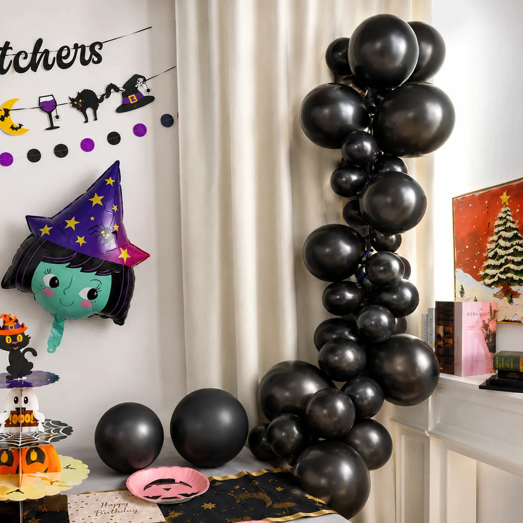 Black balloon arch for Halloween birthday party with witch foil balloon, table runner, pink pumpkin plate and little witch decorations