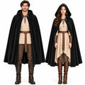 A man and a woman stand side by side wearing black hooded cloaks with brown leather wrist guards and belts.