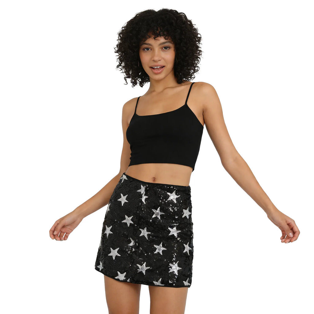 A woman models the black mini skirt with silver star sequins from the front with her hands on her hips against a white background.