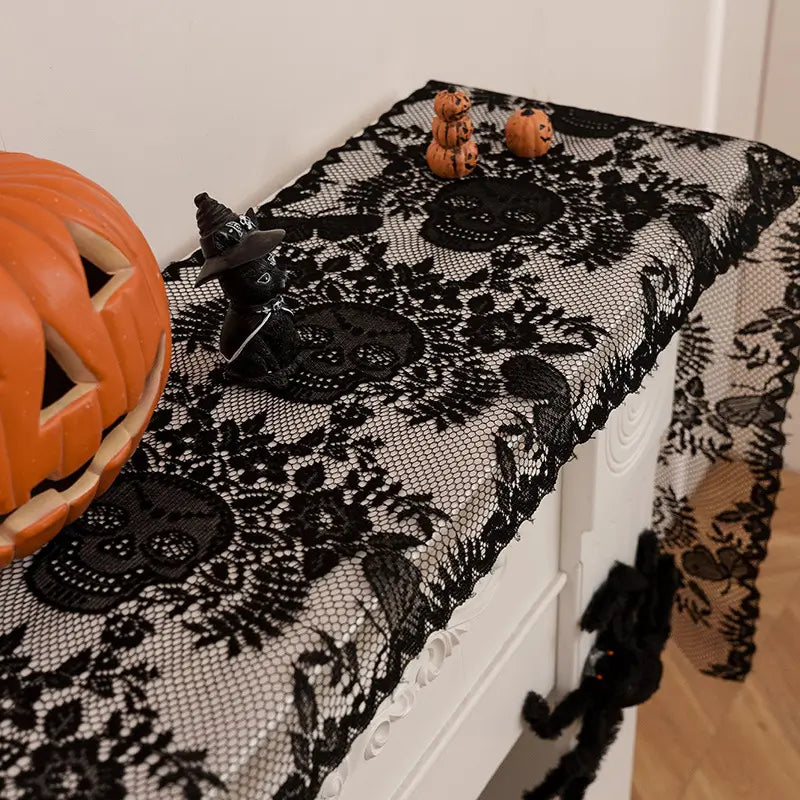 Black skull lace Halloween table runner draped over a console table with pumpkin and black cat decorations.