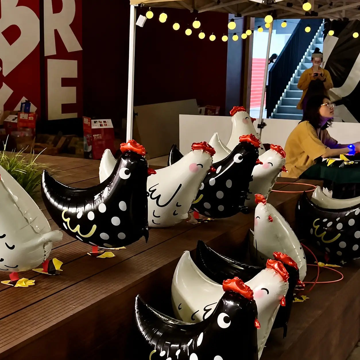 Black and white chicken foil balloons displayed at a party booth with string lights