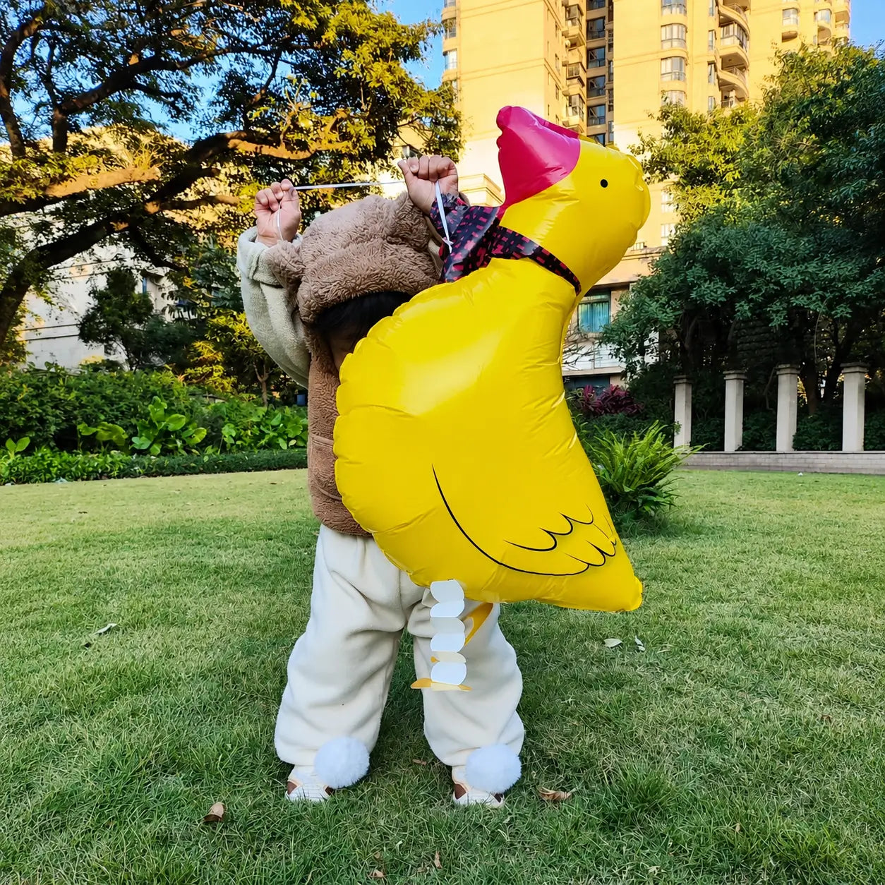 Child holding a large yellow duck-shaped foil balloon in an outdoor garden