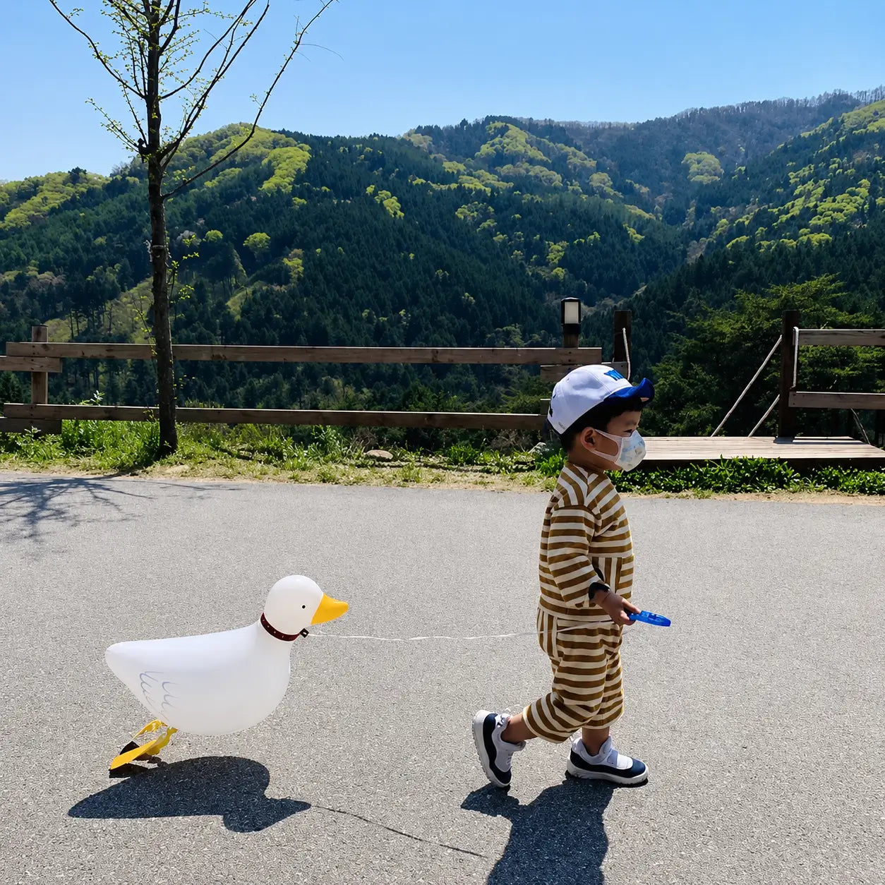 Child walking outdoors with a white duck-shaped foil balloon on a mountain road