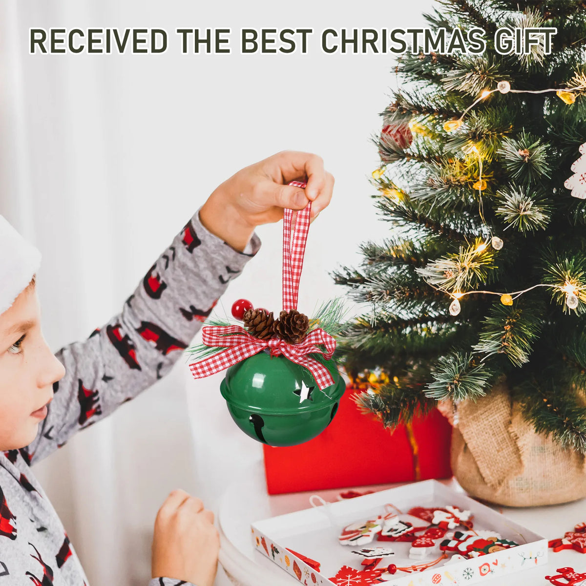 Child hanging the Green jingle bell ornament on a Christmas tree beside wrapped gifts