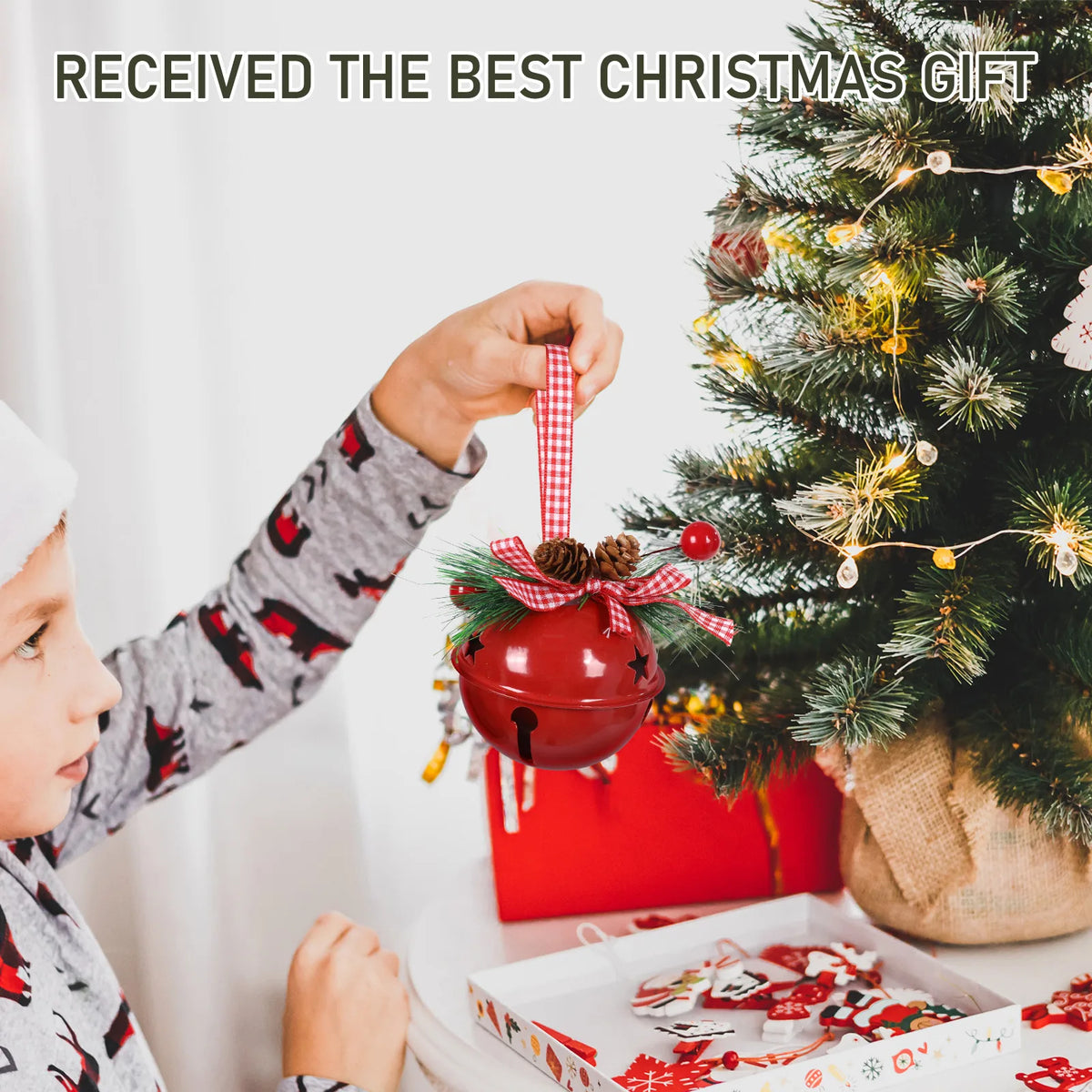 Child hanging the Red jingle bell ornament on a Christmas tree beside wrapped gifts