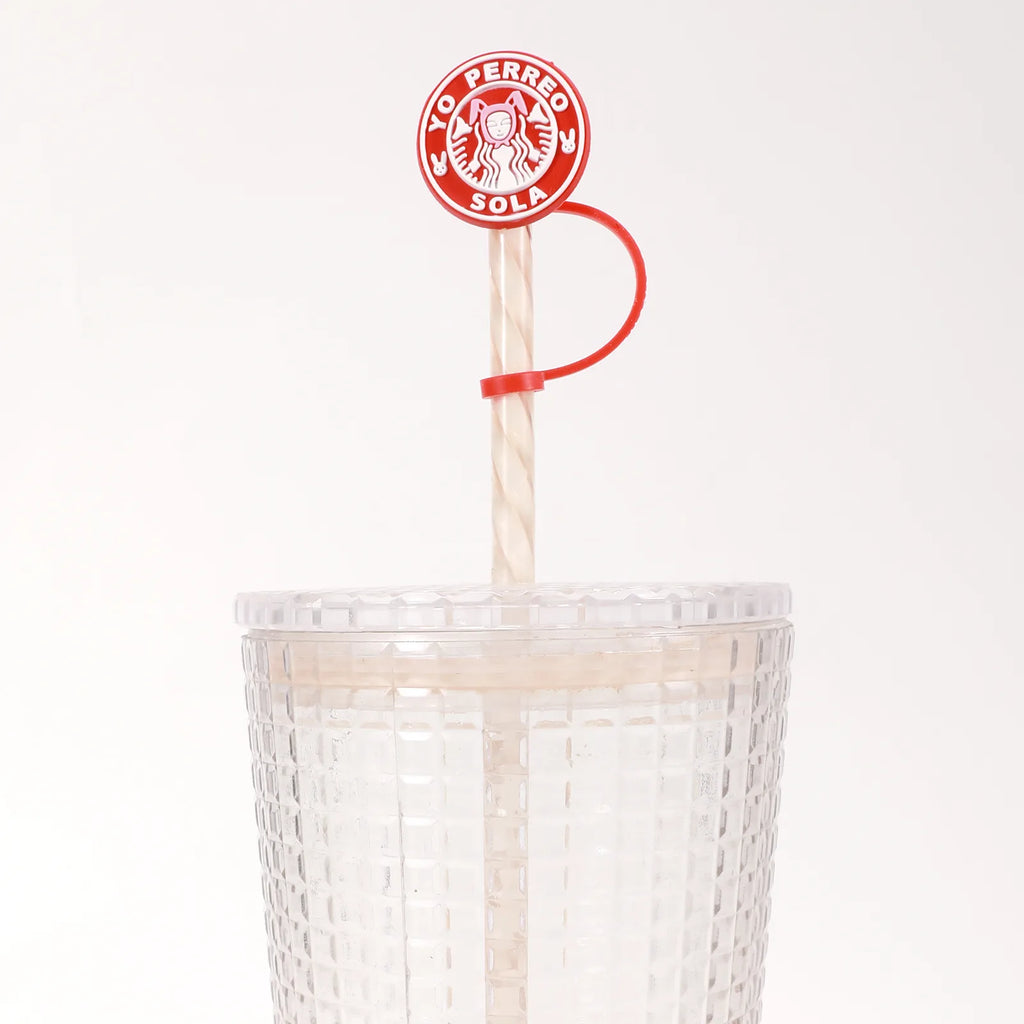 Close-up of a red circular straw cover fitted on a demonstration straw, showing the cap, connecting tether and retaining ring above a cup.