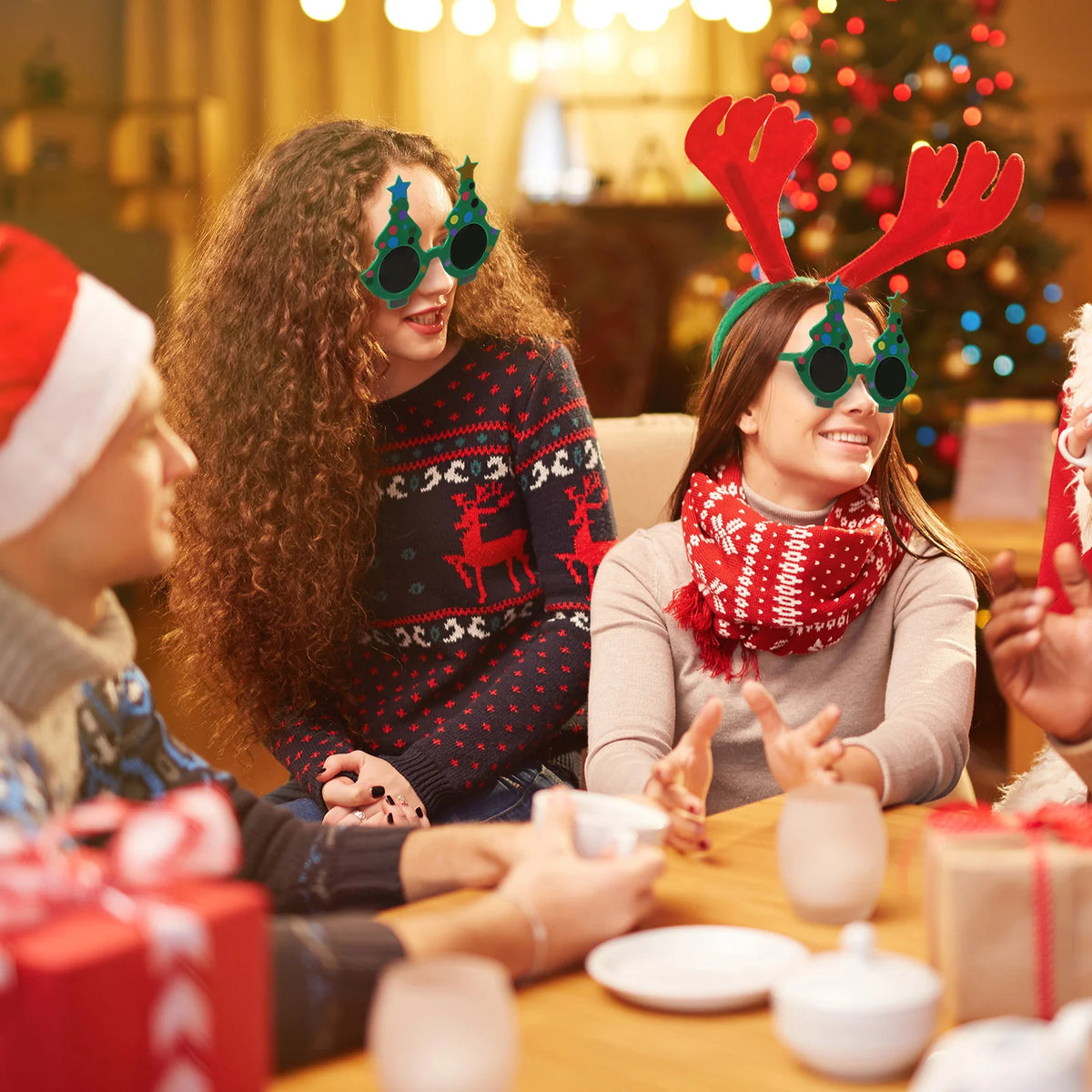Two people wear green tree glasses at a holiday table.