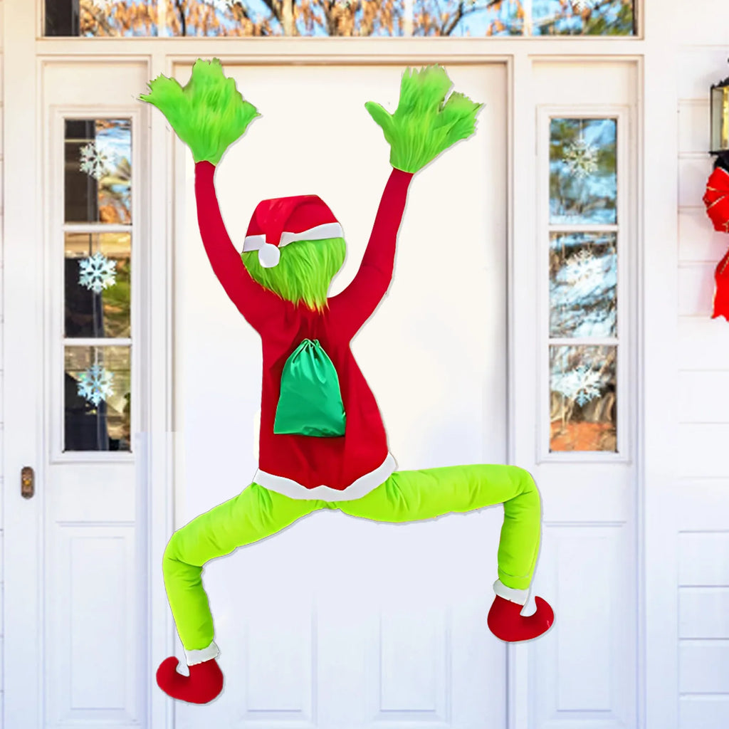 Green furry climbing Christmas character decoration (Inspired by the Grinch) hanging on a white front door with arms raised high