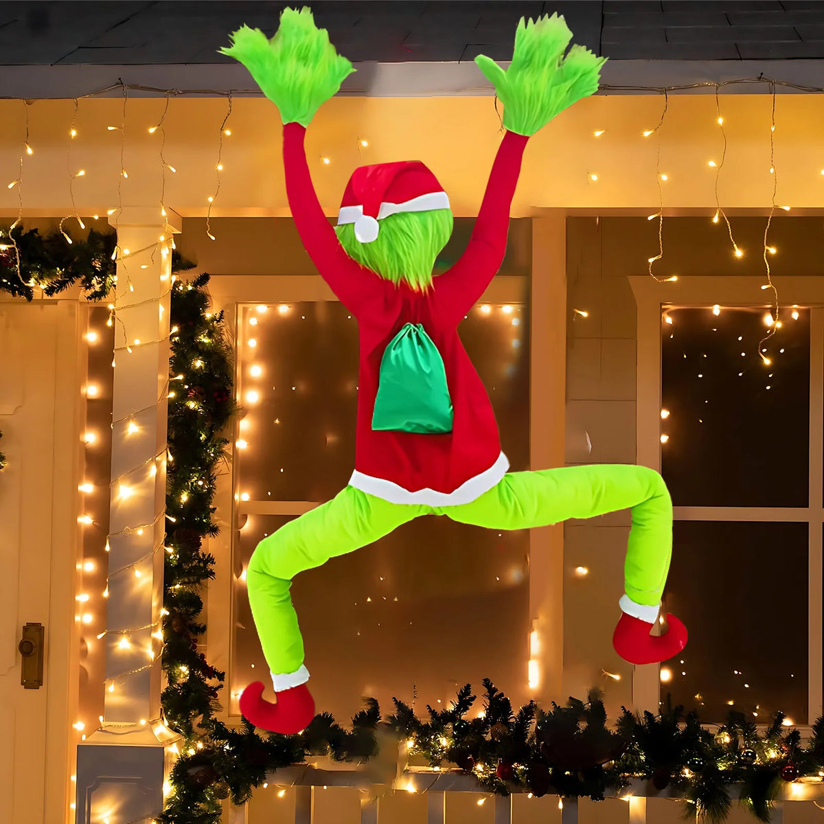 Green furry climbing Christmas character decoration (Inspired by the Grinch) hanging from a window frame decorated with warm string lights
