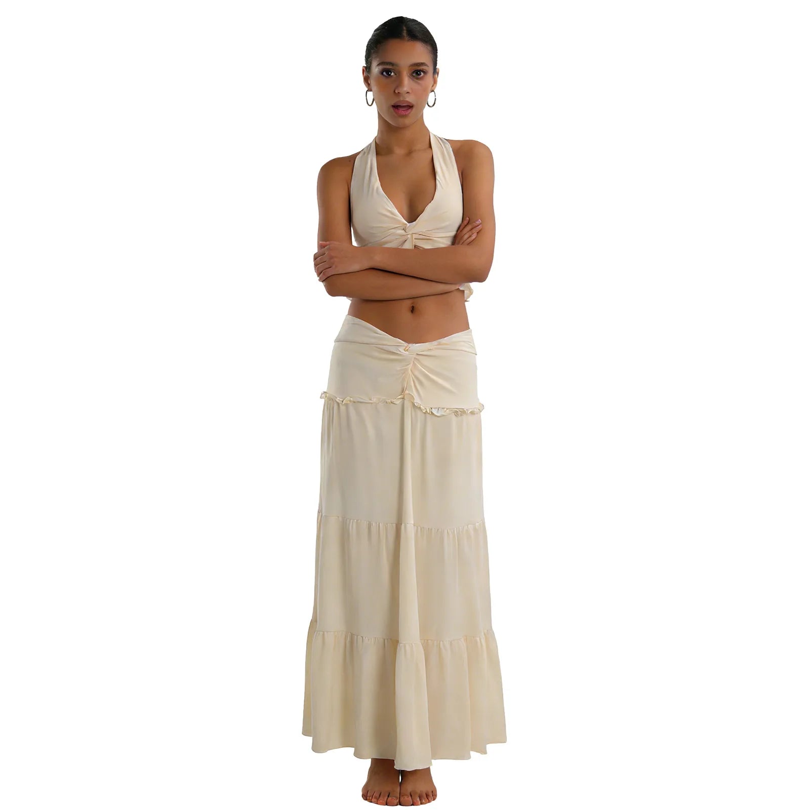 A woman models the cream halter top and maxi skirt set from the front with her arms crossed against a white background.