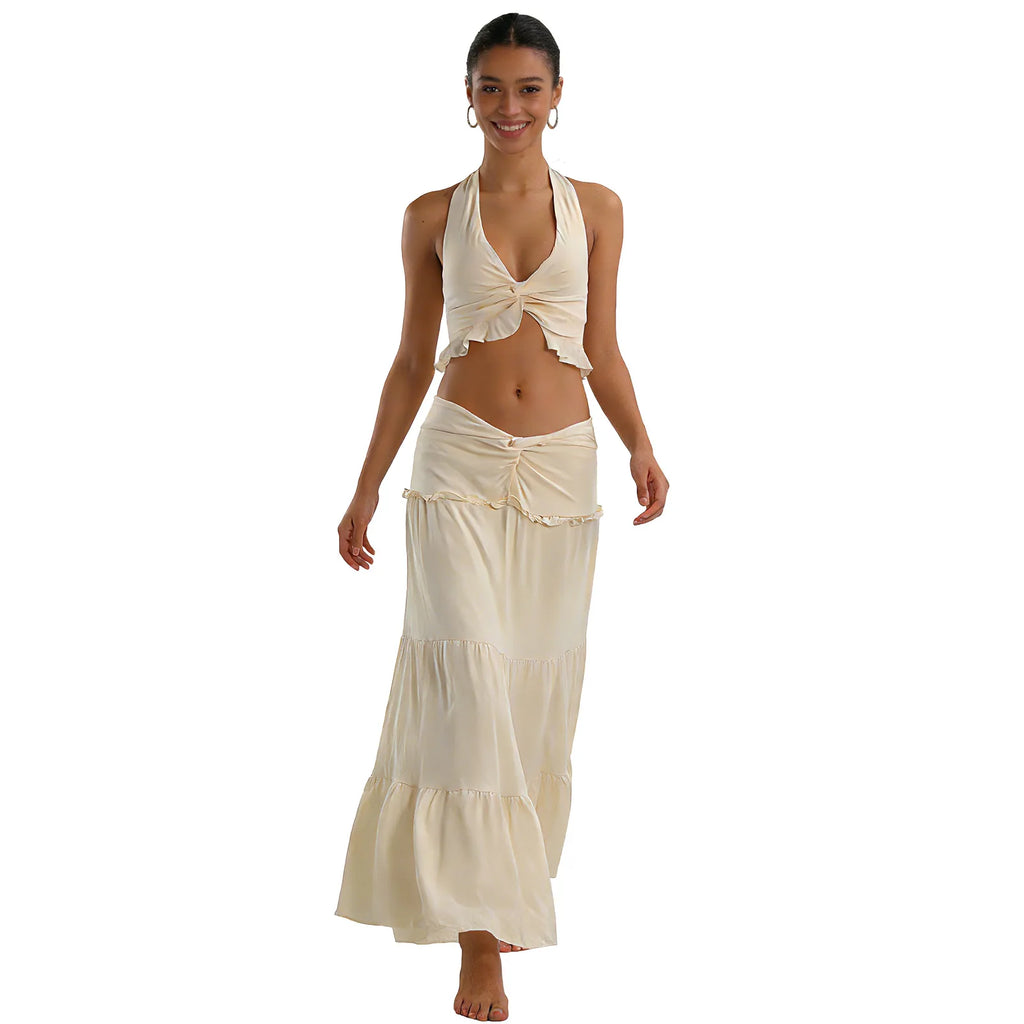 A woman models the cream halter top and maxi skirt set in a walking front pose against a white background.