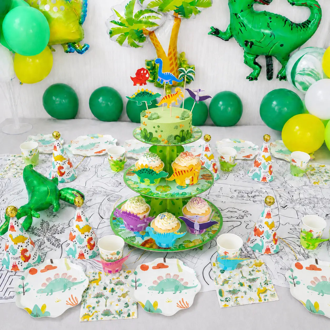 Dinosaur party table decorations with matching plates, cups, napkins, party hats, cake toppers and a three-tier cake stand.