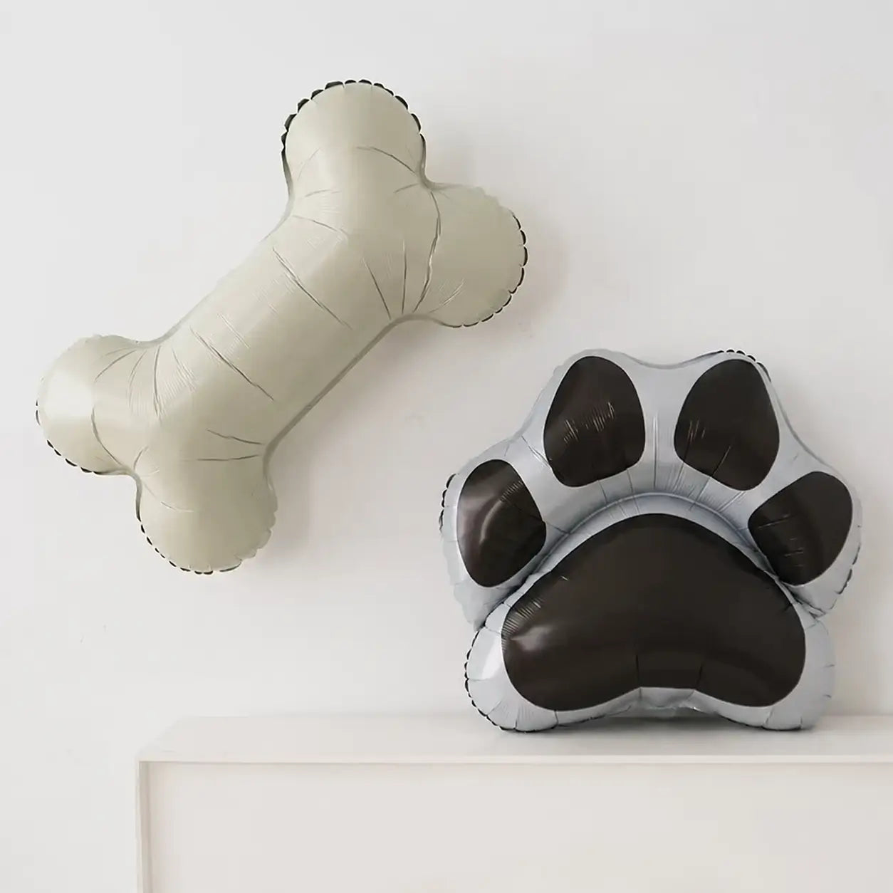 Dog bone and paw print foil balloons displayed on a white shelf for puppy birthday party decorations and pet themed celebrations.