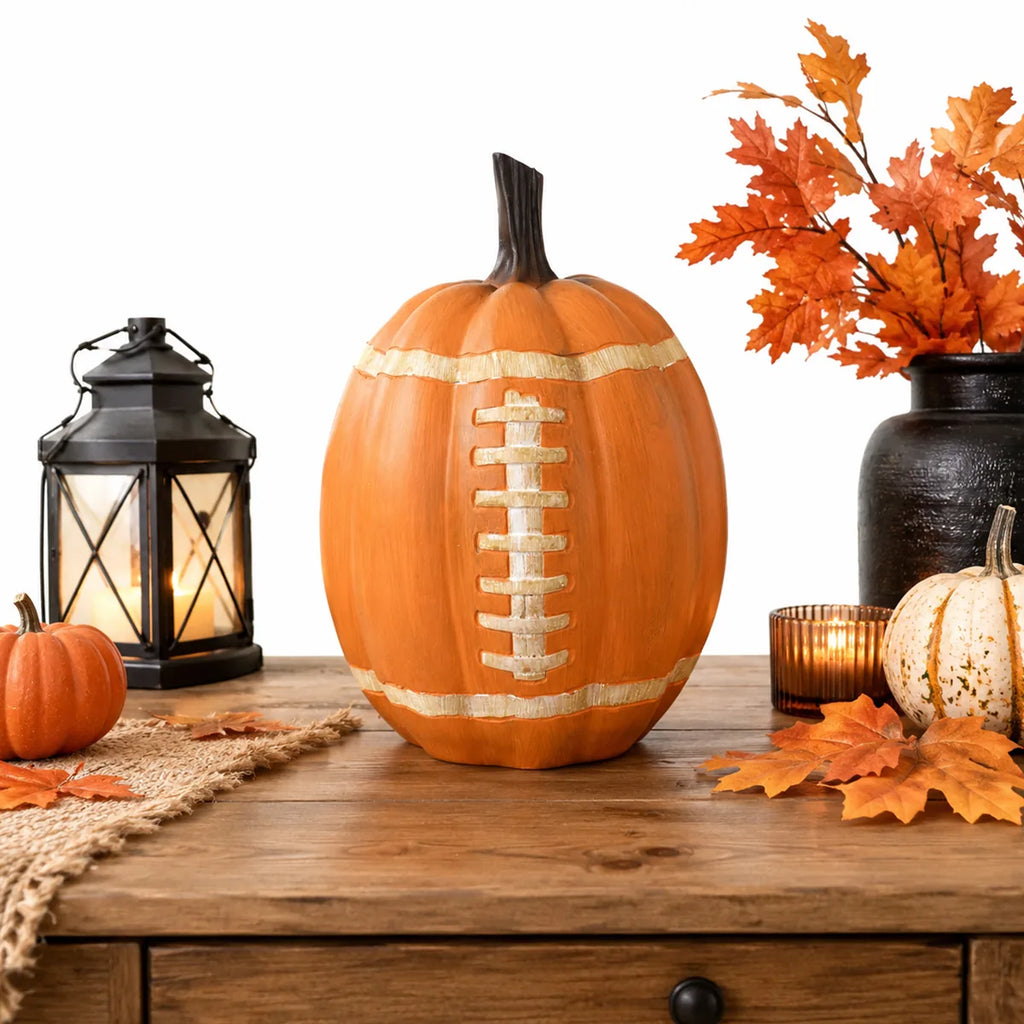 Football pumpkin displayed on a wooden table with lantern and autumn leaves.