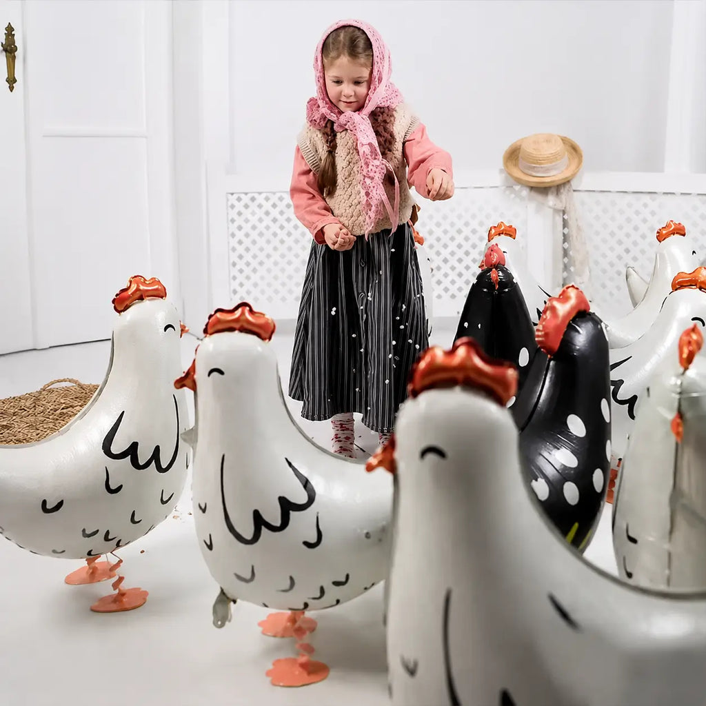 Little girl playing with white chicken-shaped foil balloons in a bright indoor setting