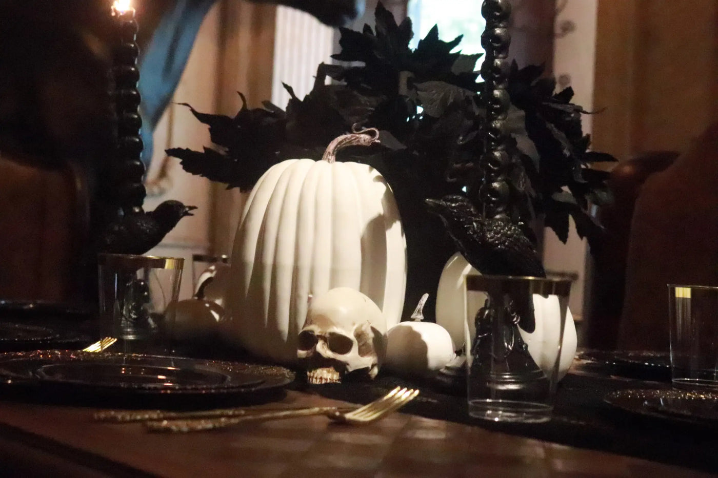 Elegant gothic Halloween centerpiece with white pumpkins, skull, black leaves, candles and black gold tableware