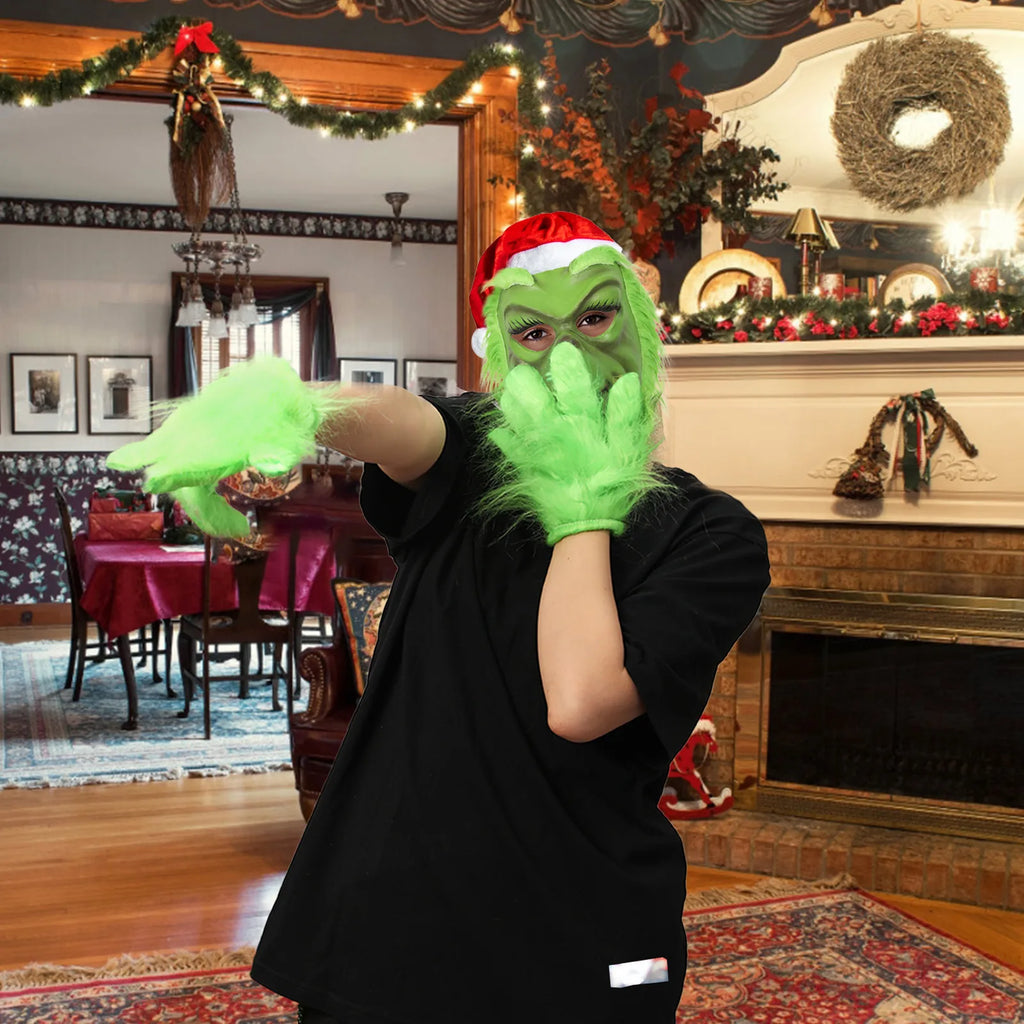 A model wearing the green monster mask reaches toward the camera in a Christmas room. The design has long lashes and a red hat.