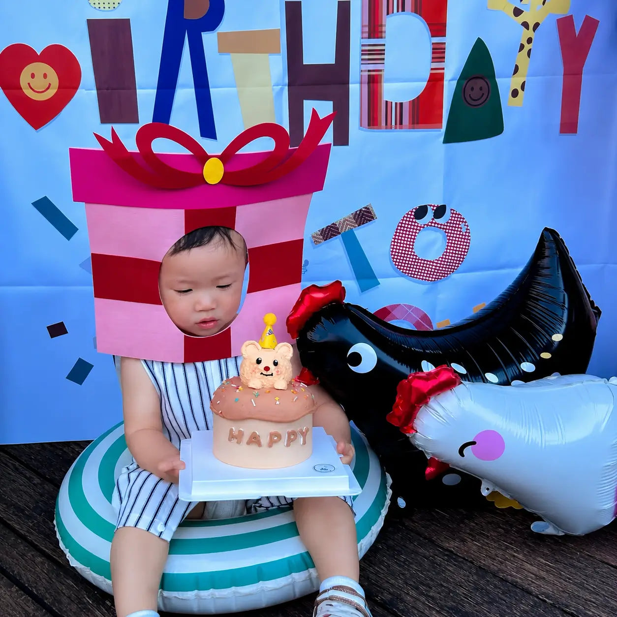 Child birthday party scene with cake, gift box costume, and chicken-shaped foil balloons