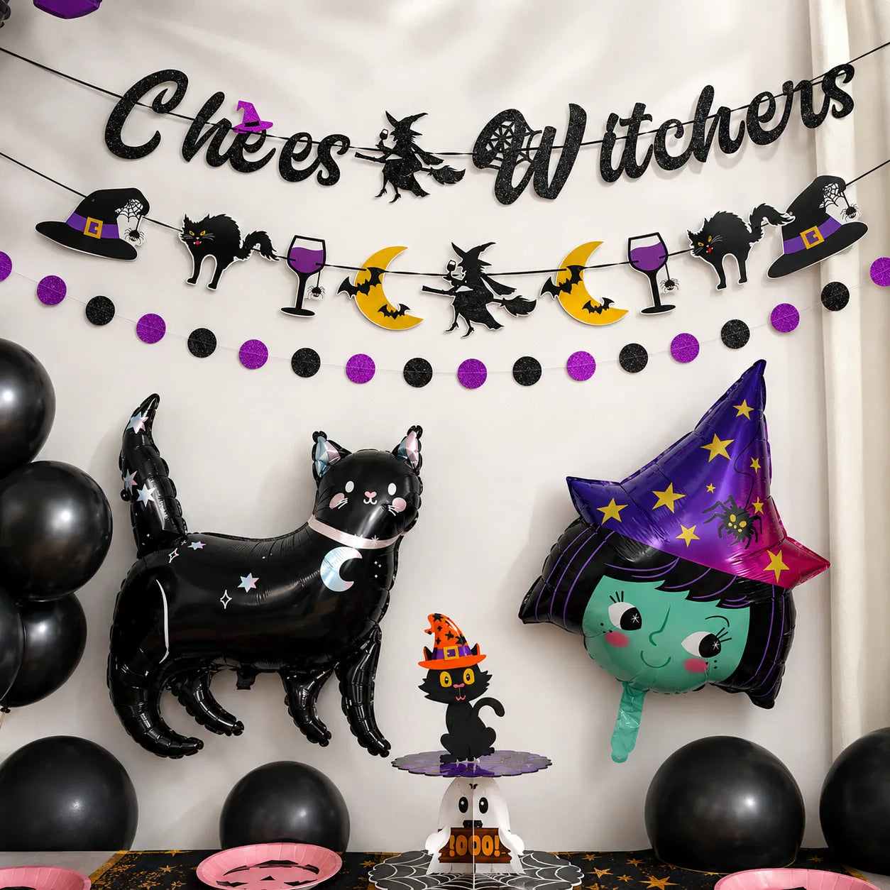 Little witch party backdrop with Cheers Witches banner, black cat balloon, witch foil balloon, black balloons and Halloween cupcake stand