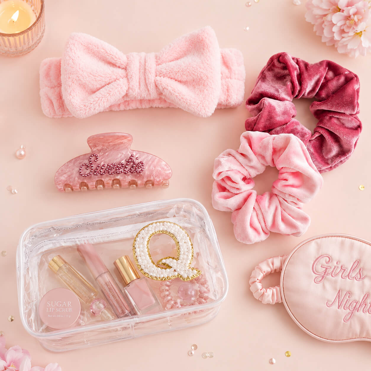 Luxury girls spa party accessory flat lay featuring clear makeup pouch, spa headband, velvet scrunchies, sleep mask, beauty products, and letter Q patch on pastel pink background