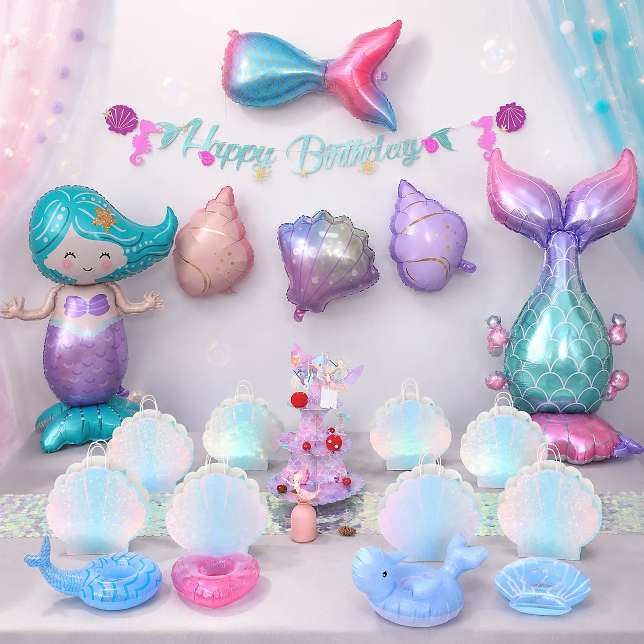 Complete mermaid birthday party supplies setup with table decorations, foil balloons, gift bags, cake stand and pool accessories