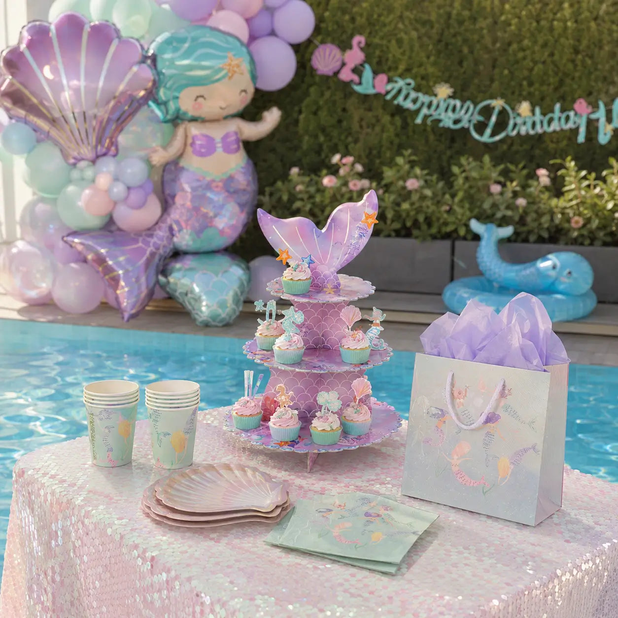 Mermaid birthday party tableware and dessert table with cake stand, paper cups, shell plates, napkins and gift bag