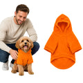 Small dog wearing an orange fleece dog hoodie with a hood, standing next to a man.