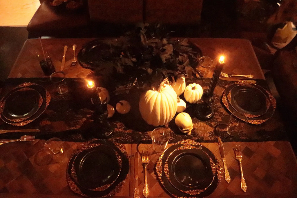 Overhead view of gothic Halloween table setting with white pumpkin centerpiece, skull, black candles, gold cutlery and black lace runner