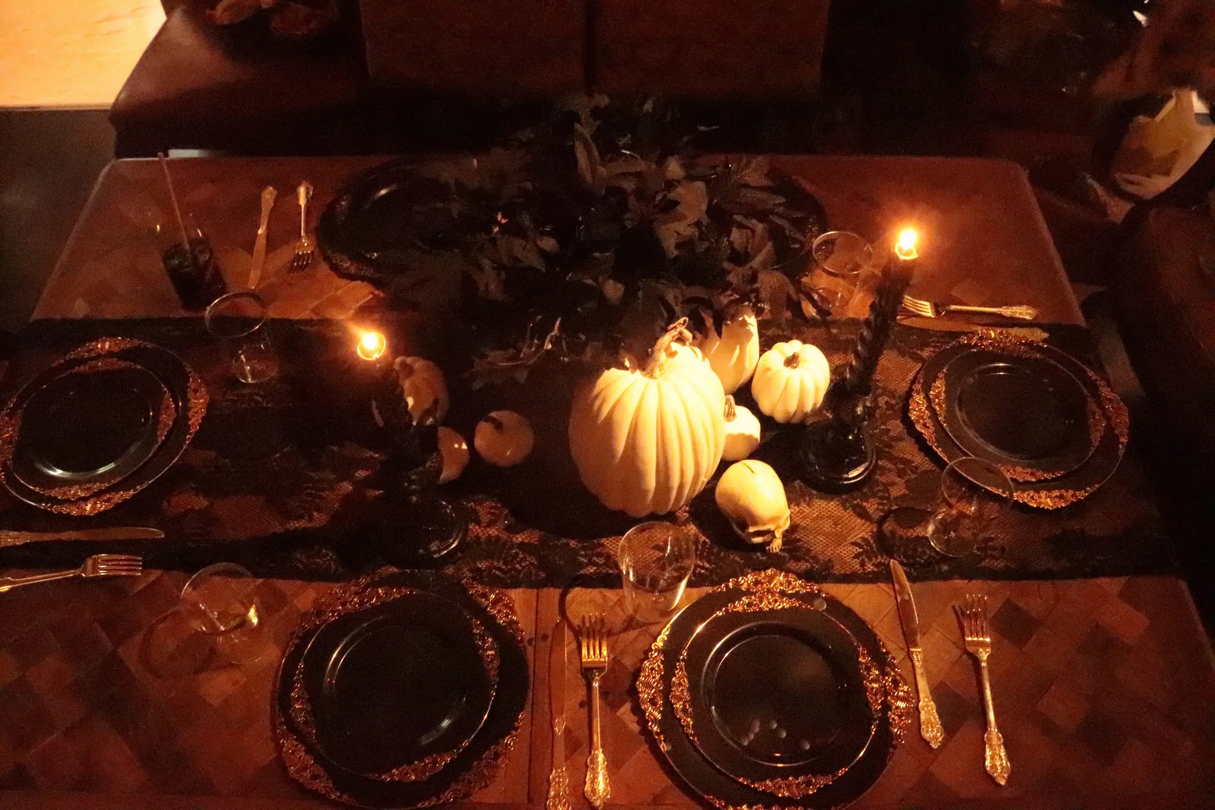 Overhead view of gothic Halloween table setting with white pumpkin centerpiece, skull, black candles, gold cutlery and black lace runner