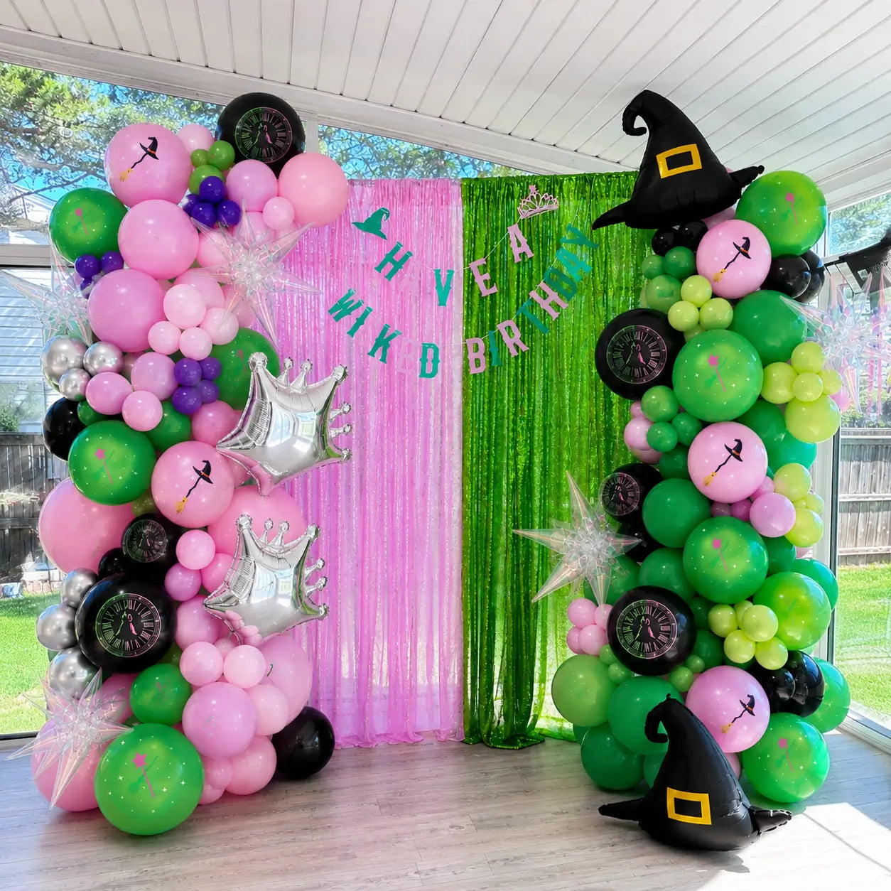 Pink and green witch birthday balloon garland backdrop with witch hat balloons, crown balloons, magic themed banner and shimmer curtain