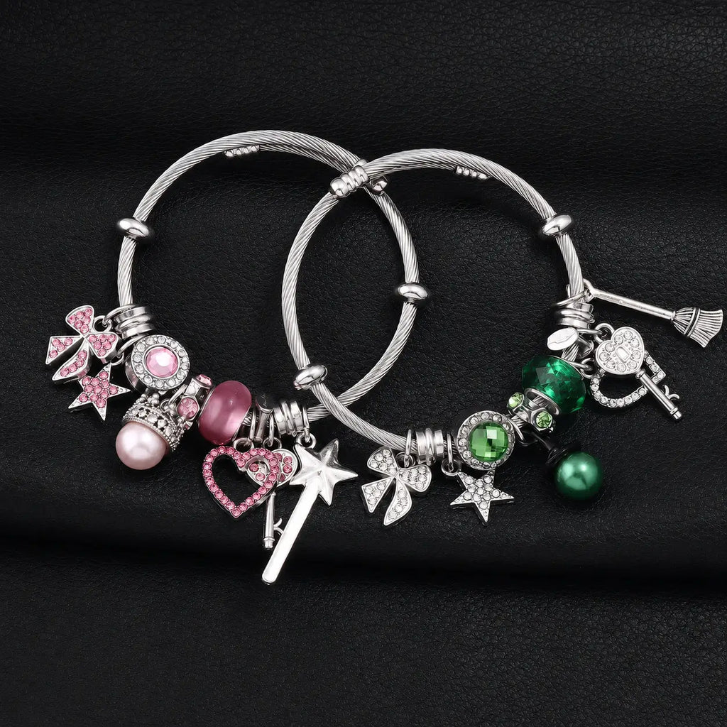 Pink and green witch charm bracelets with silver cable bands, hearts, stars, bows, keys, wand, broom, and rhinestone charms on a black background.