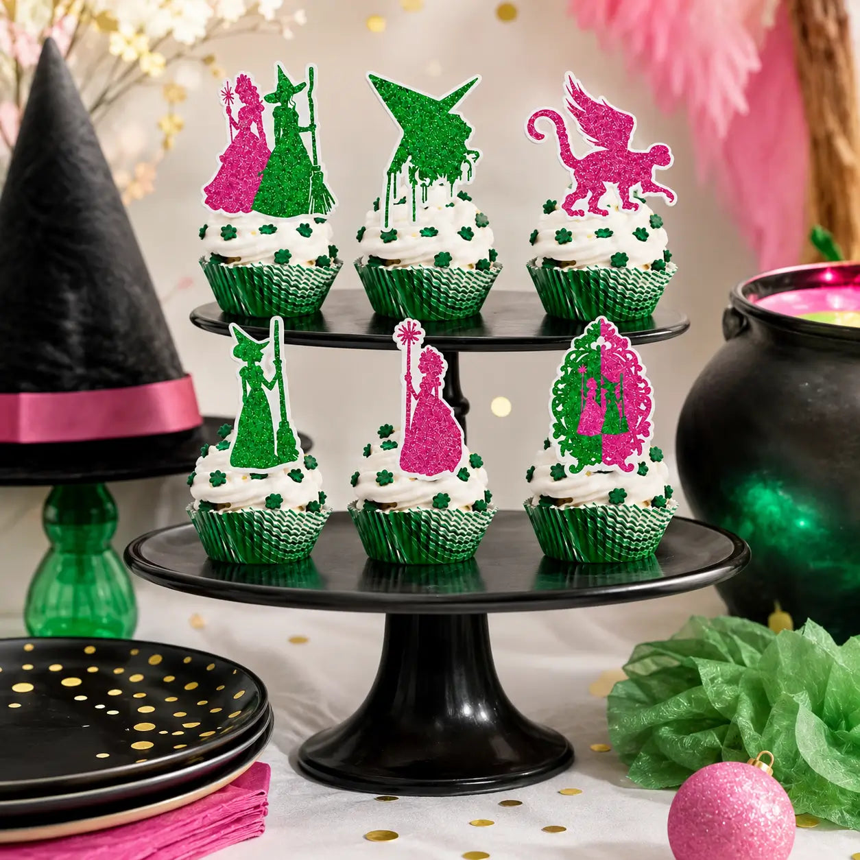 Pink and green glitter witch cupcake toppers displayed on cupcakes with black cake stands, witch hat, cauldron, plates, and party decorations.