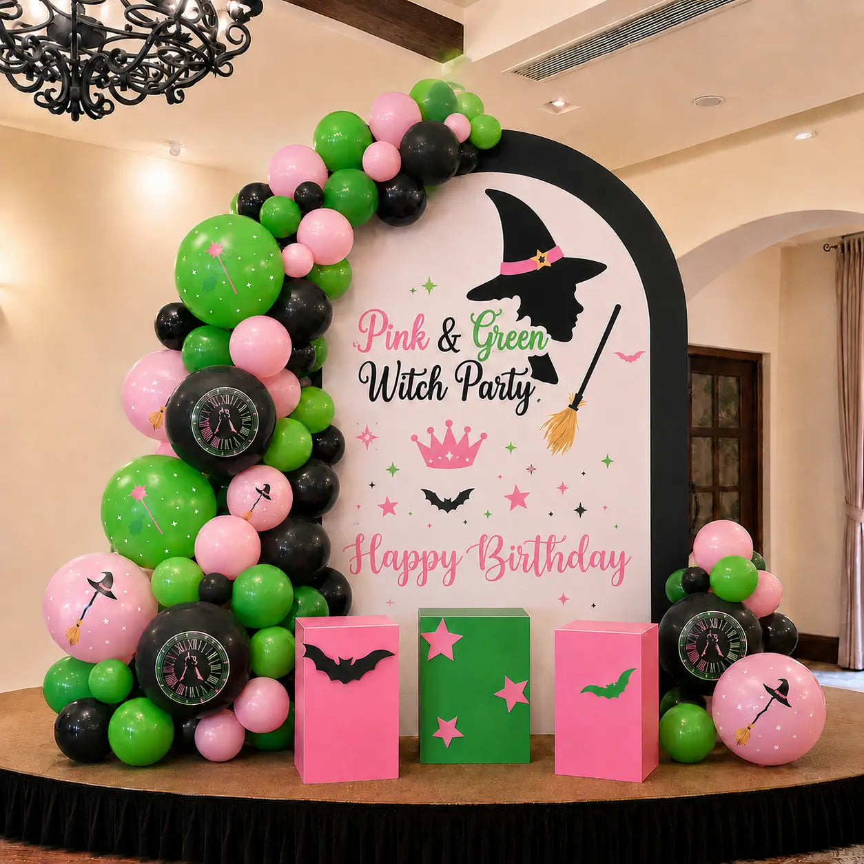 Pink and green witch party birthday backdrop with balloon arch, witch silhouette, broom, crown, bats, magic themed balloons and pink green party props