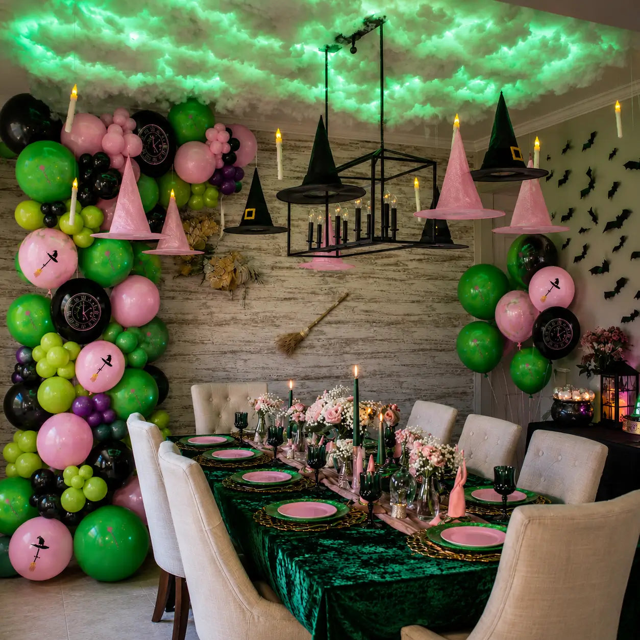 Pink and green witch party decorations with balloon garland, hanging witch hats, floating candles and magical tableware