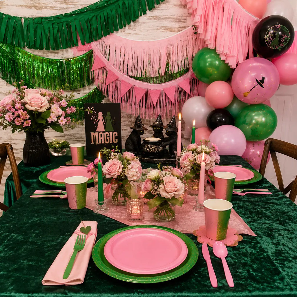 Pink and green witch party table setting with balloon backdrop, fringe garlands, candles, flowers, pink plates and magic themed party decor