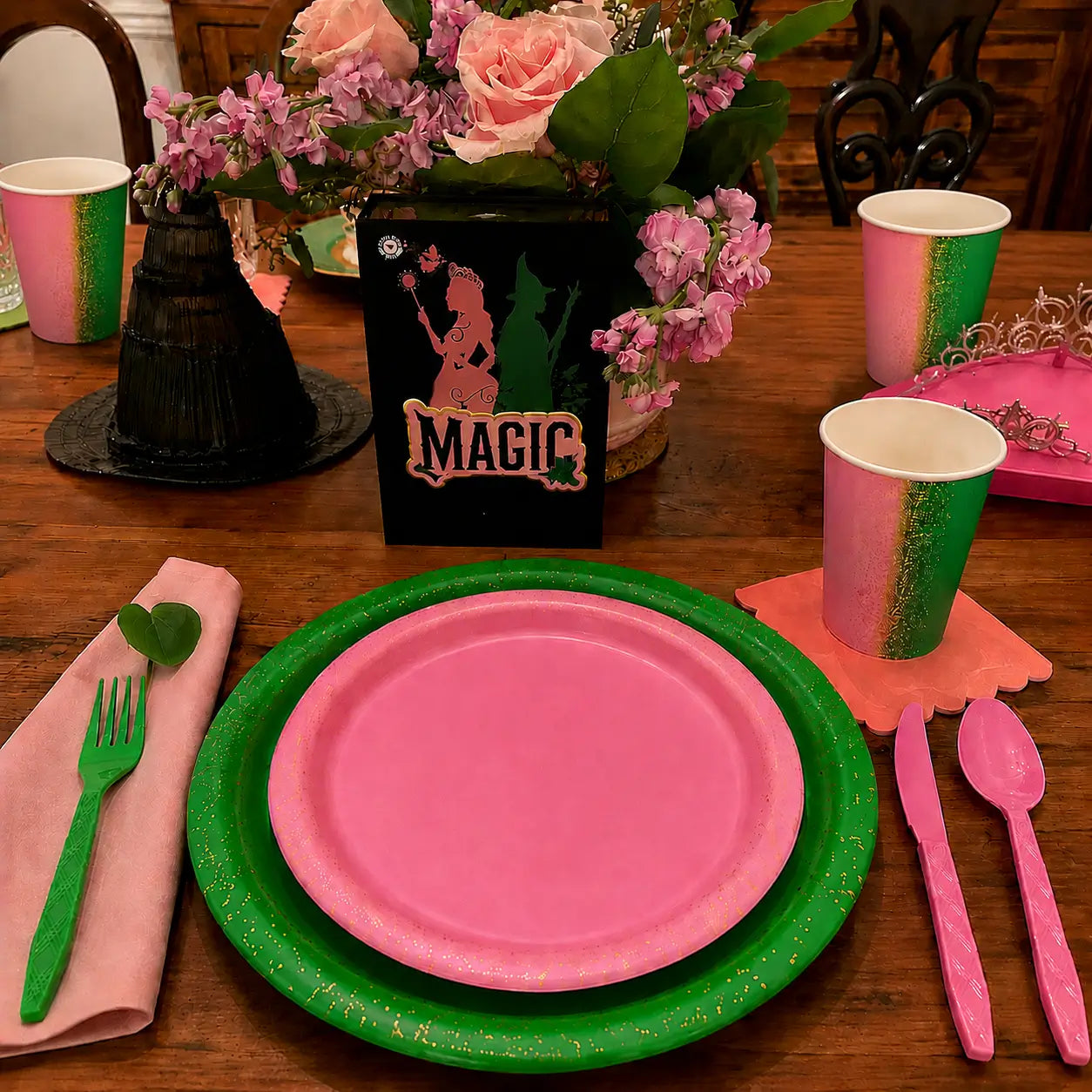 Pink and green witch party tableware close up with pink plates, green plates, matching cups, pink cutlery, green cutlery and magic themed centerpiece