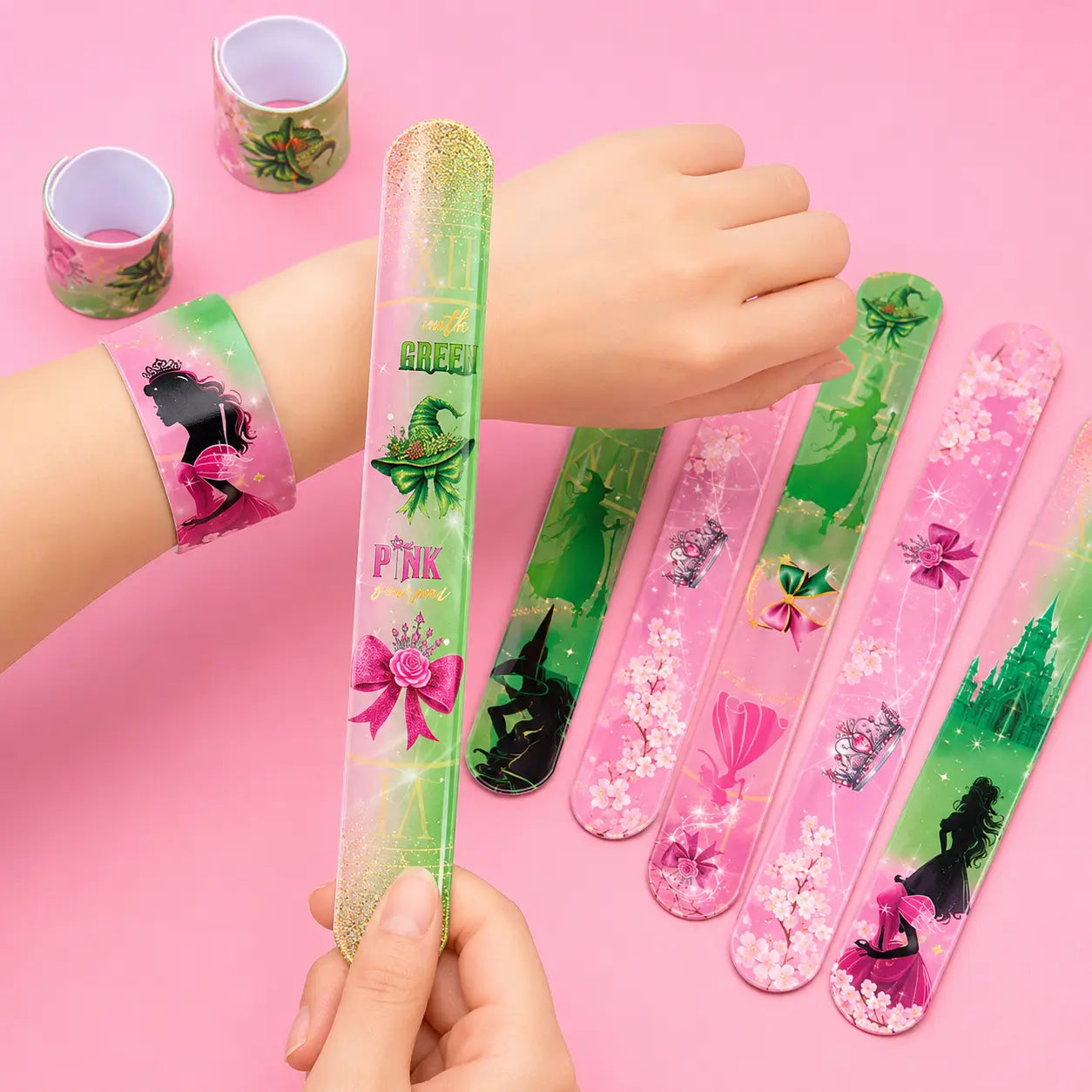 Pink and green witch and princess slap bracelets shown on a wrist with matching bracelet designs on a pink background.