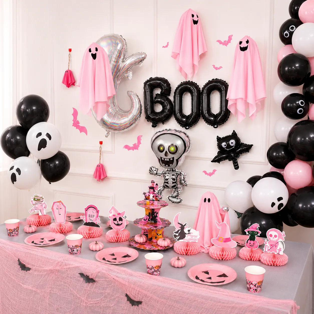Pink Halloween party table with pumpkin plates, cups, ghost decorations and balloon backdrop