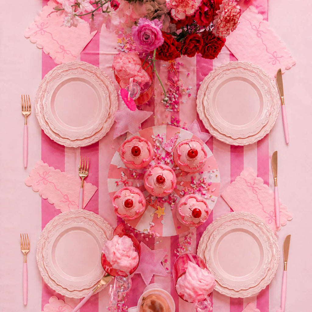 Pink party table setting with pink plates, rose gold cutlery, floral centerpiece, candles, confetti and elegant pink striped table decor
