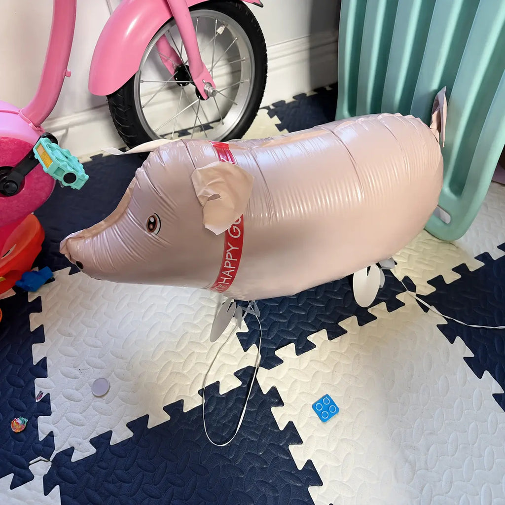 Pink pig walking foil balloon displayed indoors on a children’s play mat