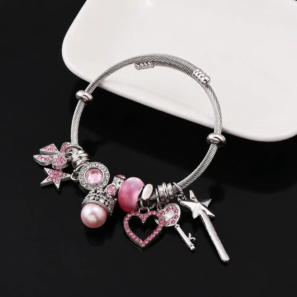 Pink and silver princess charm bracelet with heart, star, bow, key, wand, crown, pearl, and pink rhinestone charms displayed on a black surface.