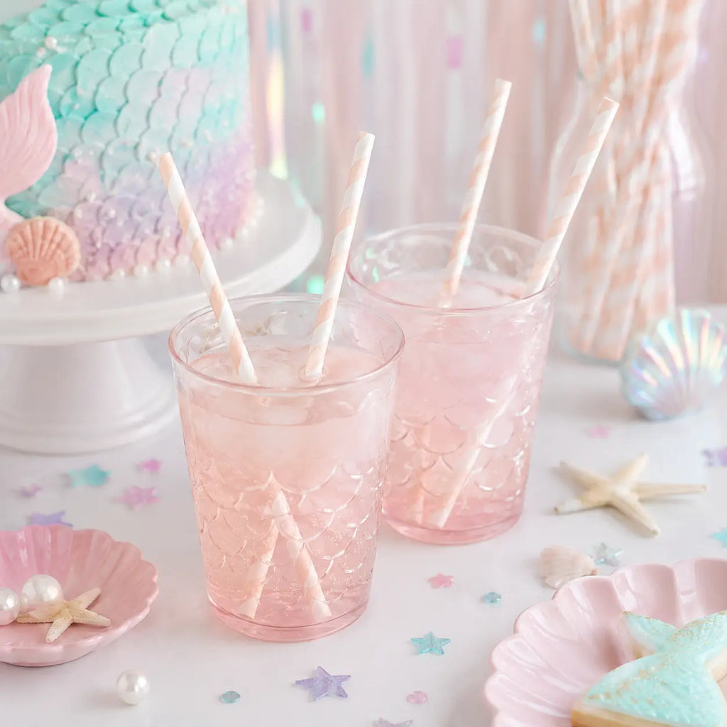 Pink striped paper straws in drinks on a pastel mermaid birthday party table with seashell decorations.
