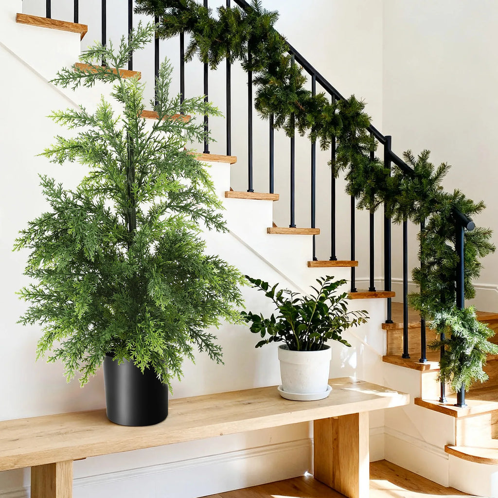 The potted tree sits on a wooden surface beside a decorated staircase.
