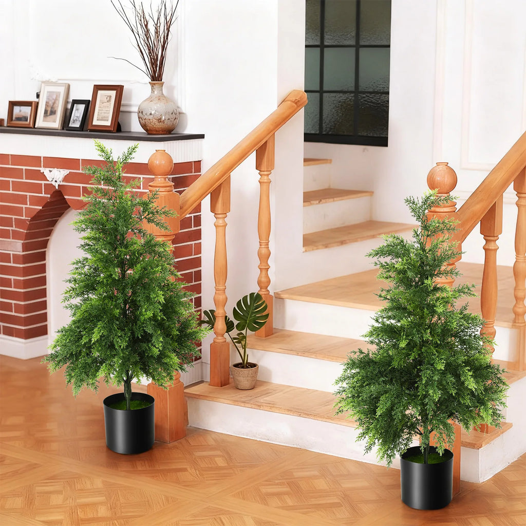 Two potted trees are styled beside a staircase in a living room.