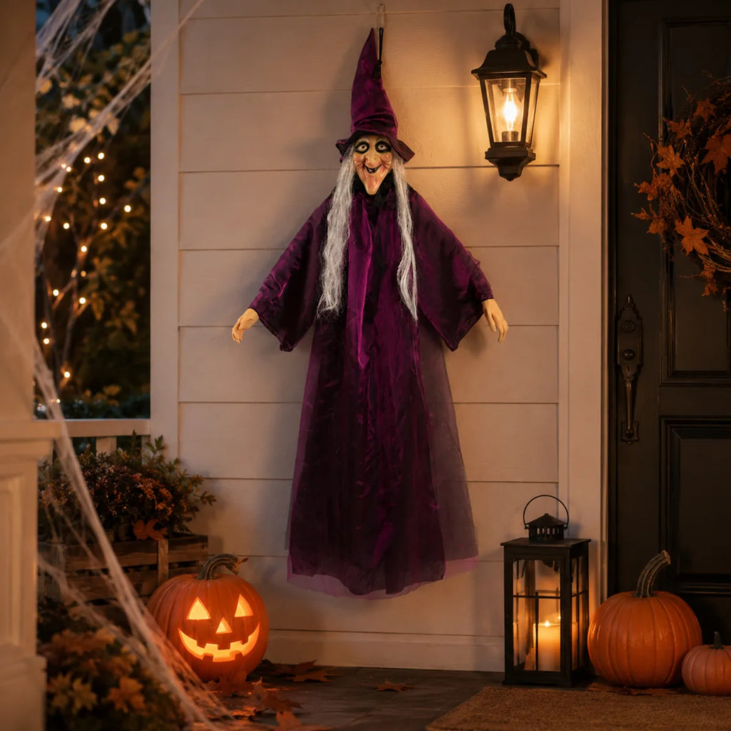 Purple hanging witch displayed beside a front door with lanterns and pumpkins.