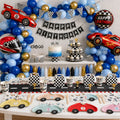 Race car birthday party decorations with a blue and gold balloon garland, checkered gift boxes and car-shaped plates