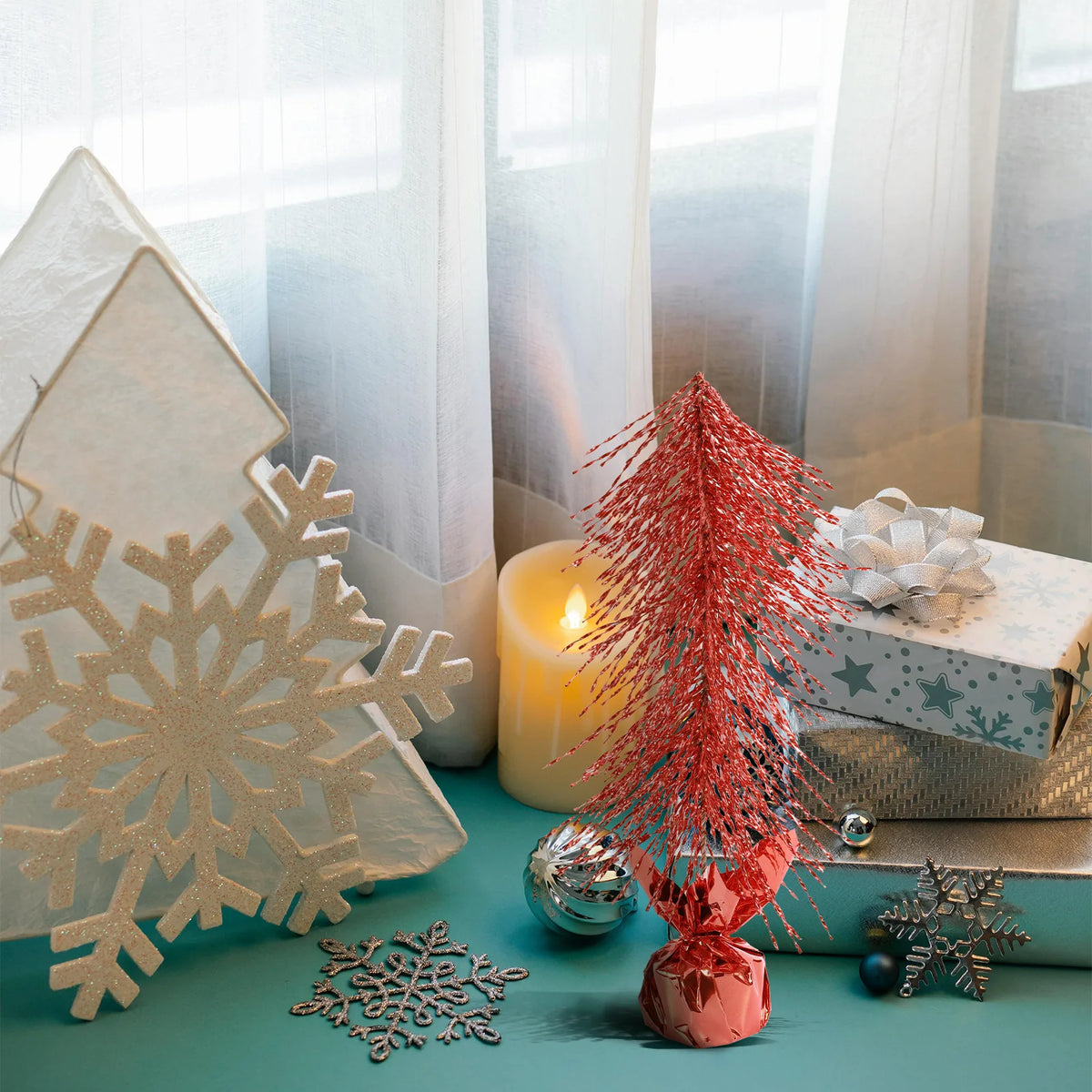 A red tabletop Christmas tree stands beside winter decorations on a blue table.