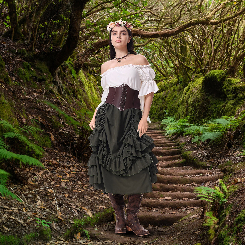 Woman in an olive green medieval peasant costume standing on a woodland path